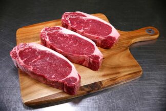 Three hand cut sirloin steaks on chopping board
